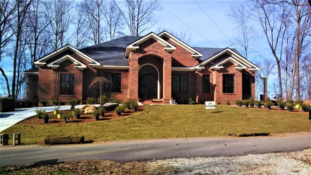 Front exterior of a custom-built all-brick home in the Lake Lanier area with multiple front gables, an arched barrel-vaulted entry portico, arched windows and fresh foundation landscaping