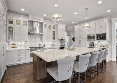Cumming, GA area kitchen remodel with white shaker cabinets to the ceiling, glass-front uppers, a large stone-topped island seating five, twin drum chandeliers, a stainless range and mosaic tile backsplash
