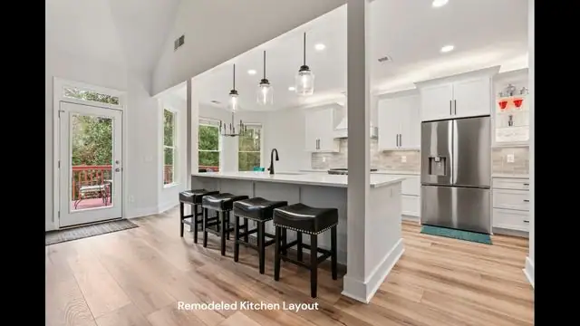 Finished open-concept kitchen remodel with white shaker cabinets, a custom range hood and a large quartz island